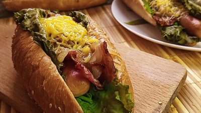 Хот-дог с беконом, листьями салата, сосиской, горчицей и сыром